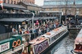 Tour boats moored on Regent`s Canal inside Camden Market, London, UK, people walking around the market